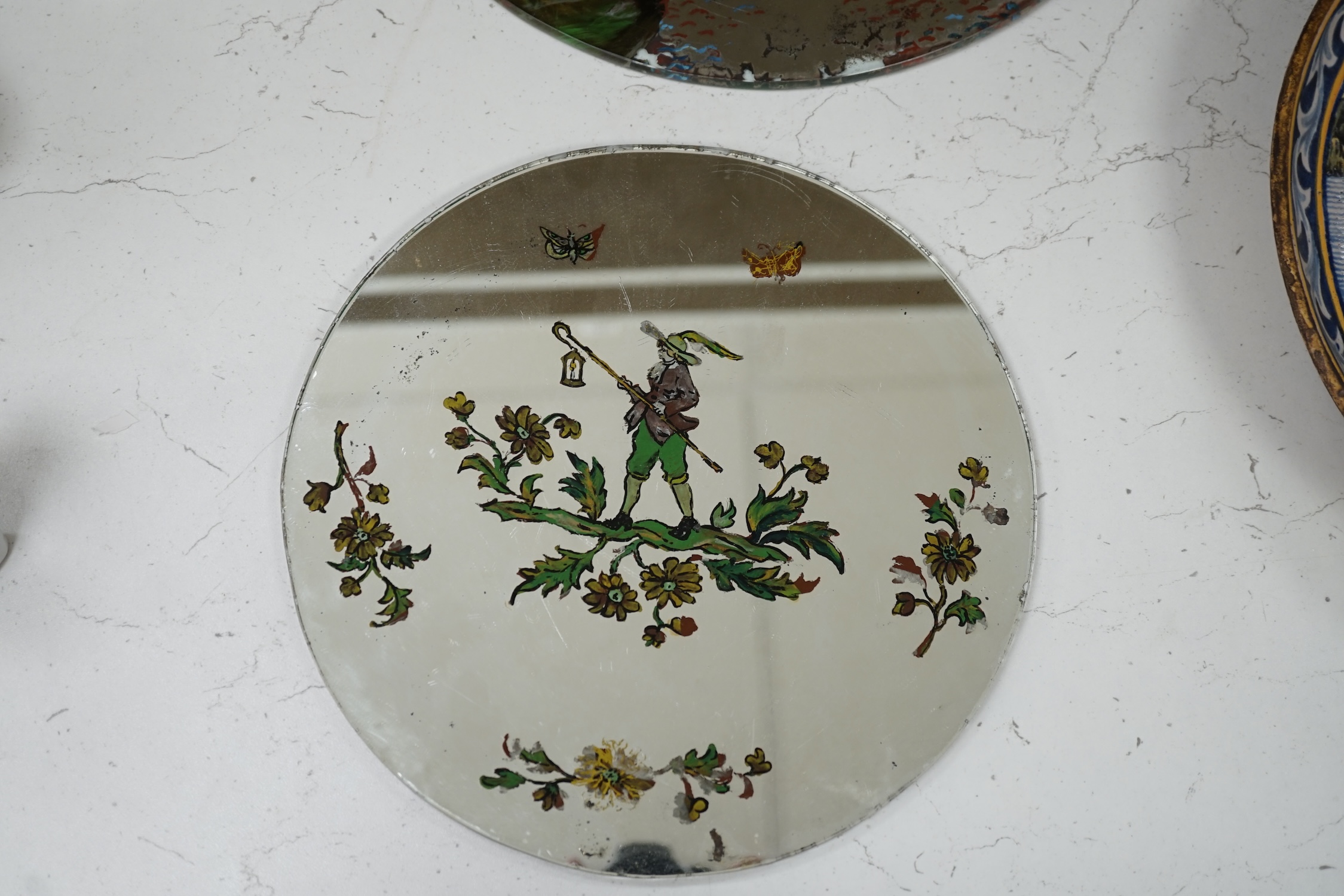 Three reverse painted mirrored glass place mats including a pair depicting landscapes with figures on horseback, largest 30cm diameter. Condition - fair